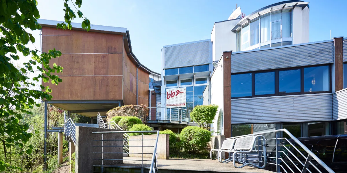 Moderner „bbz“-Gebäudekomplex mit Holzfassade und Metallgeländern unter klarem blauem Himmel.
